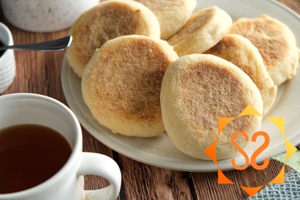 A plate of English muffins next to a cup of tea