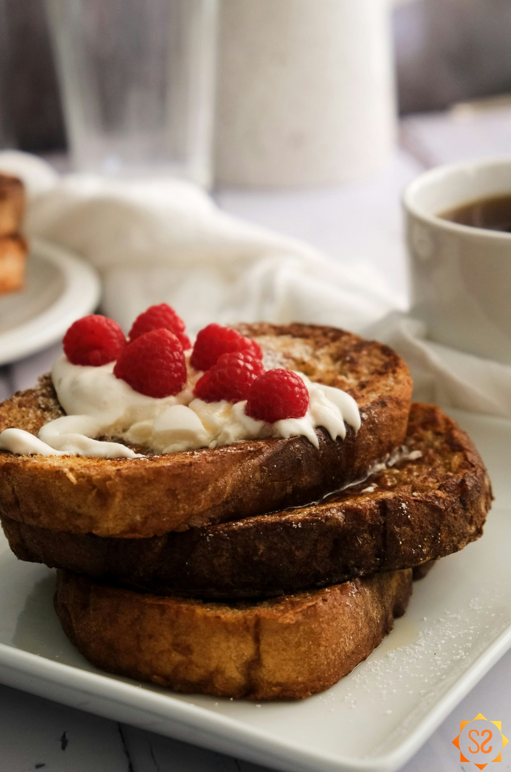 A stack of French toast with a cup of coffee and a pitcher of juice in the background