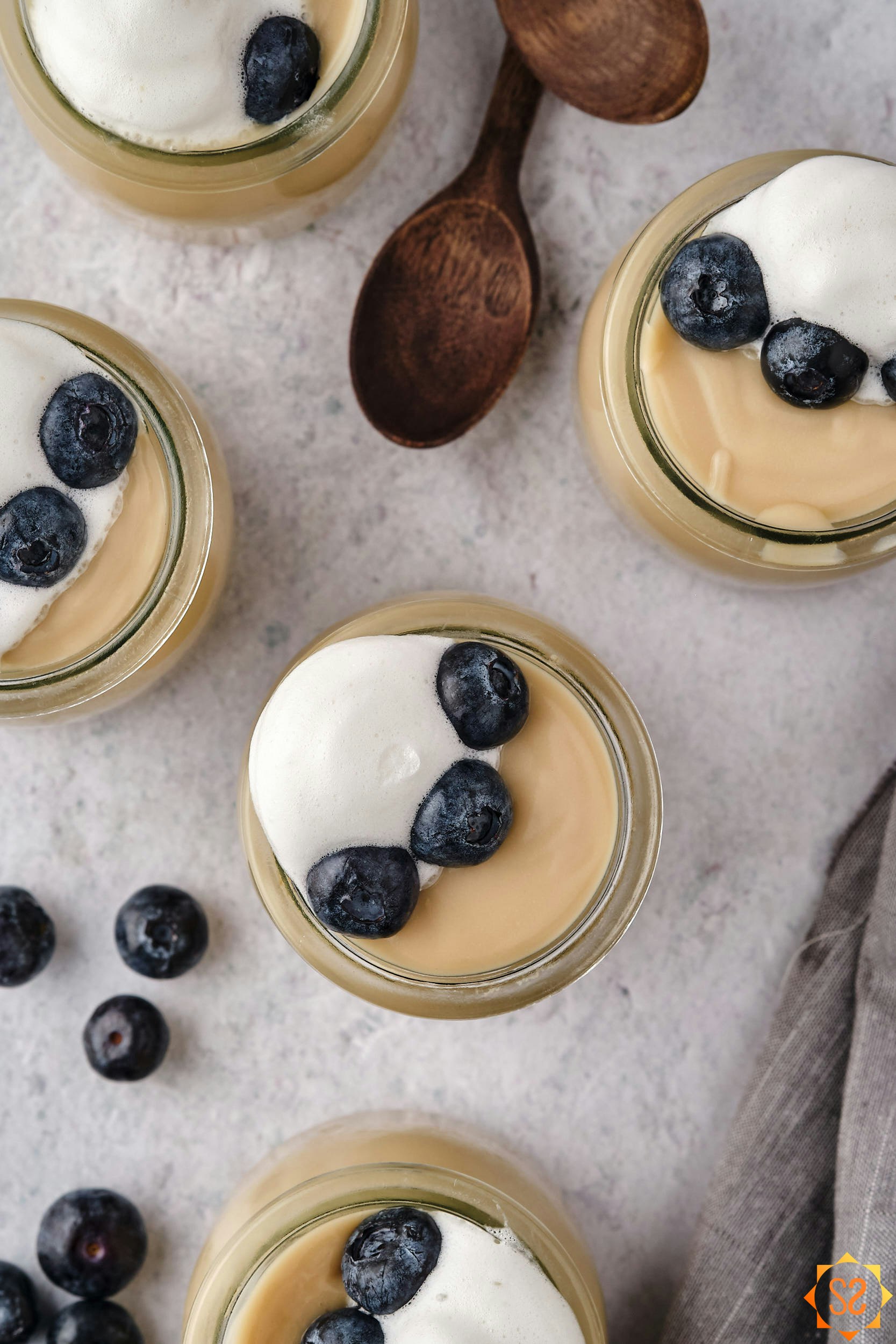 A top-down view of several jars of vegan vanilla pudding with blueberries and spoons.