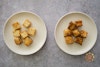 Two plates of tofu pieces, one baked in the oven and the other stir-fried in a wok