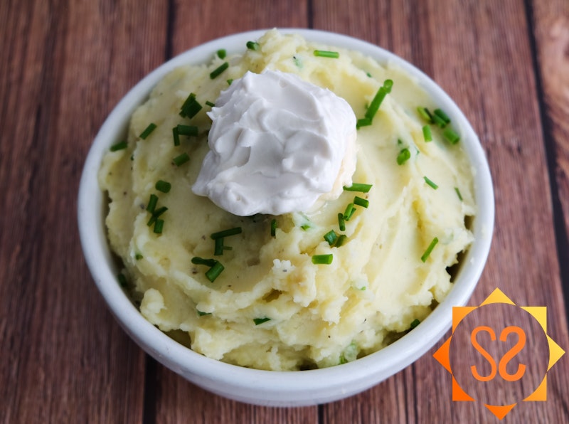 A bowl of vegan sour cream mashed potatoes with chives and sour cream on top