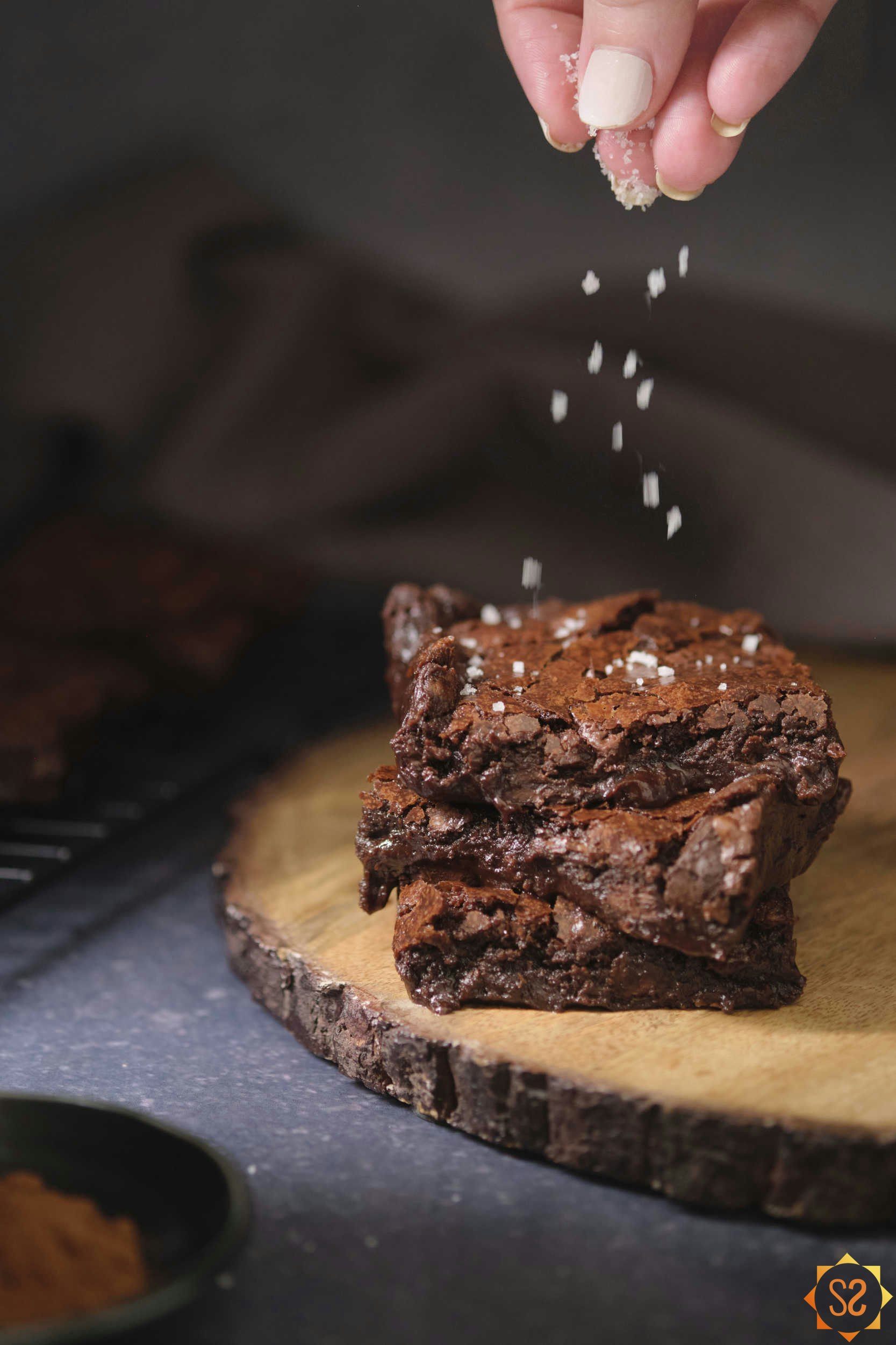 A stack of brownies with a hand sprinkling fleur de sel on top. 