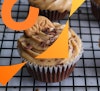 A closeup of a chocolate cupcake with cookie butter frosting, topped with shaved chocolate and a speculoos cookie