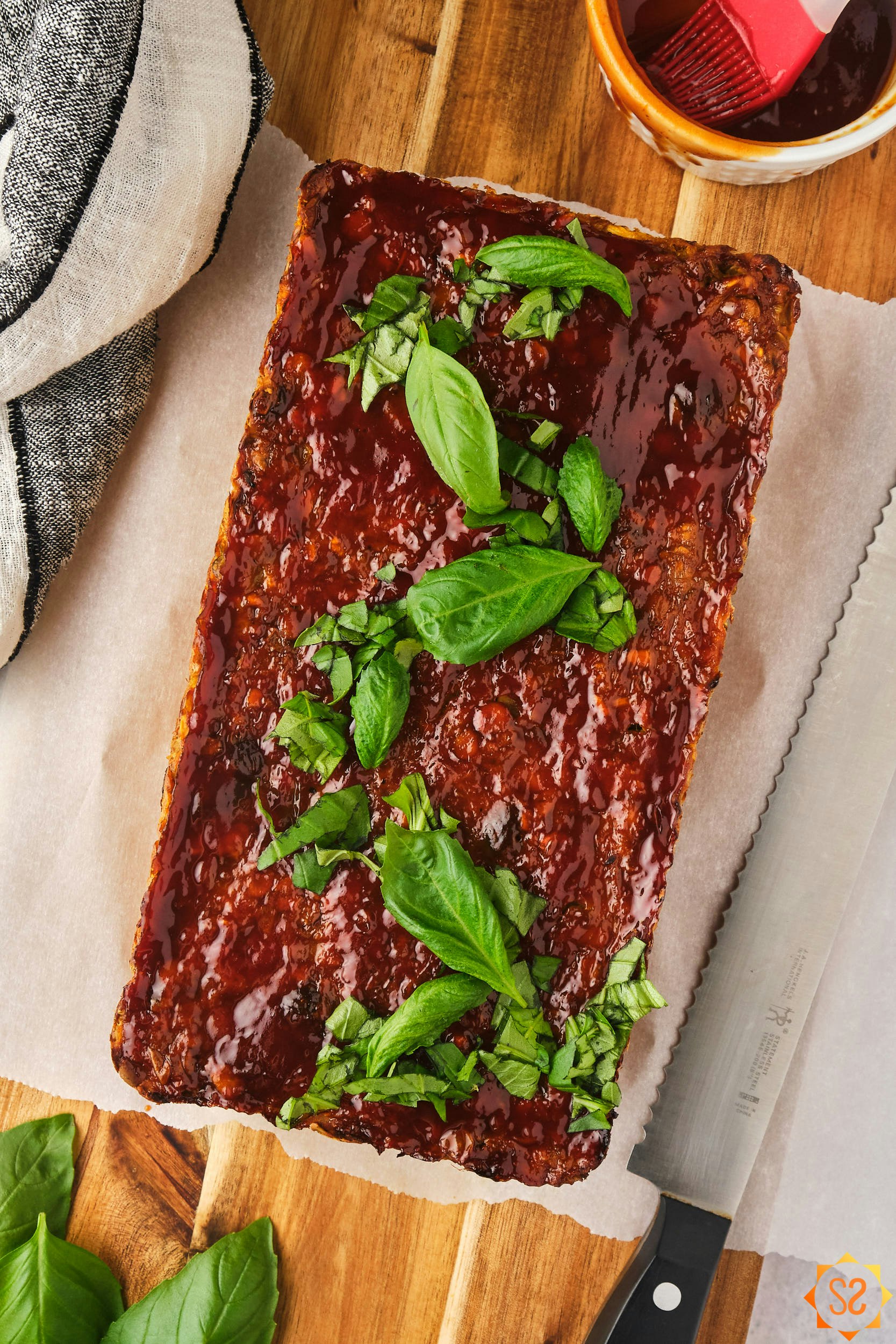 Lentil loaf on a cutting board with a knife, basil, and glaze.