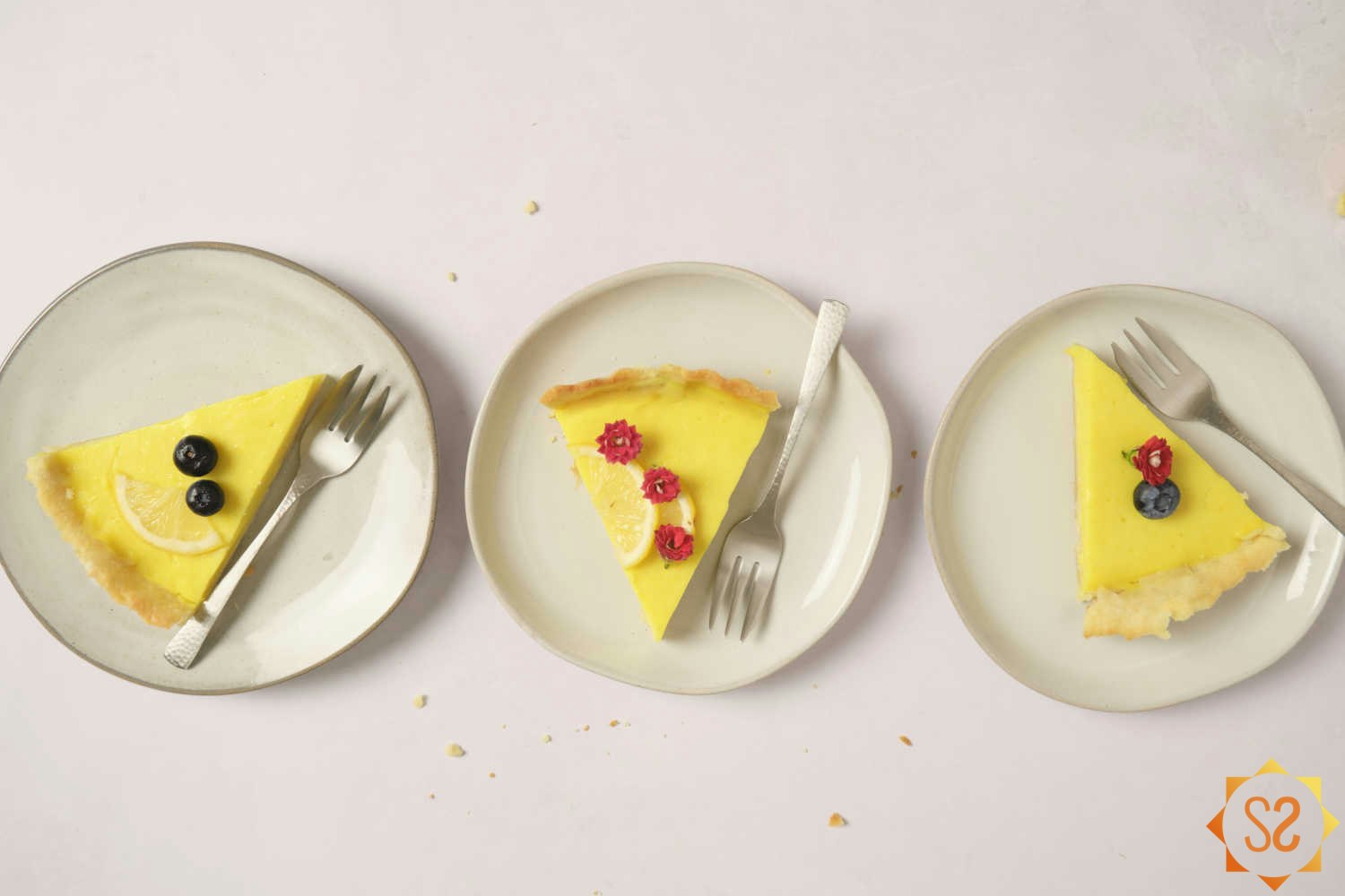 Three slices of vegan lemon tart on three plates with forks lined up from right to left.
