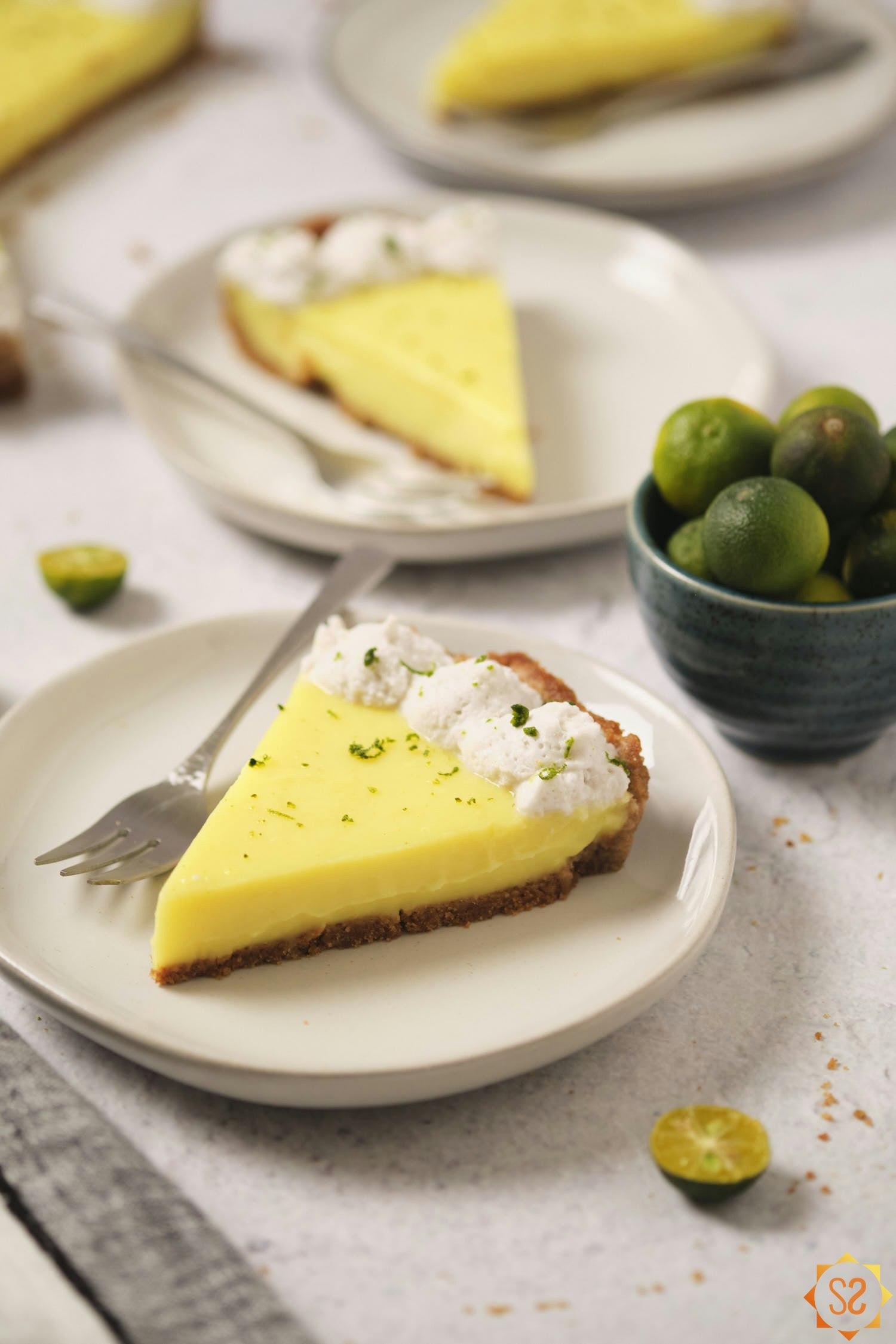 A slice of vegan Key lime pie on a plate, with more plates of pie in the background.