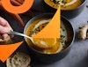 A hand dipping a spoon in carrot pumpkin soup with cashew cream