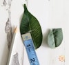 A marking pencil, a leaf that's been marked with a marking pencil with a measuring tape on top, and a leaf that's been cut 