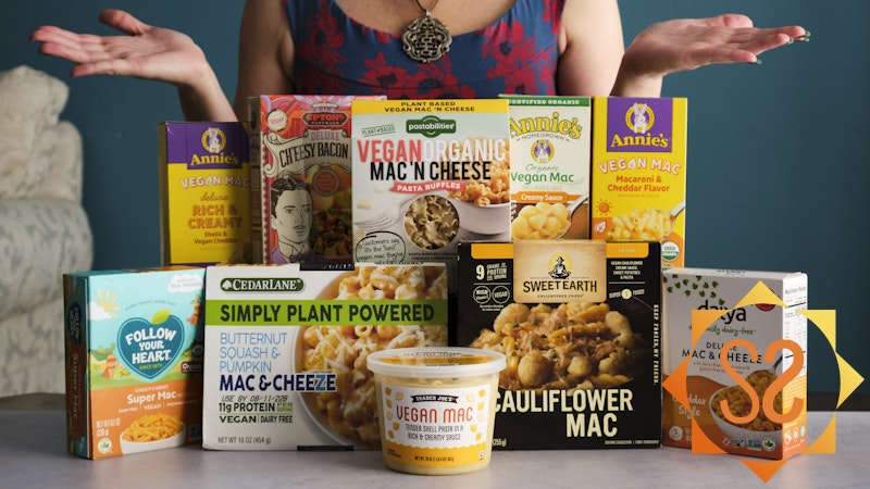 Ten vegan mac and cheese boxes on a table with a person behind them with palms up